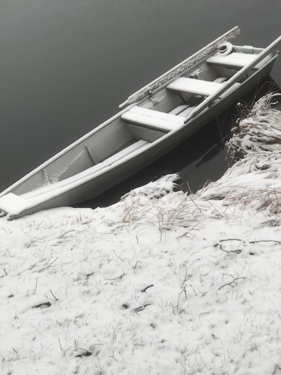 snow covered boat on riverbank